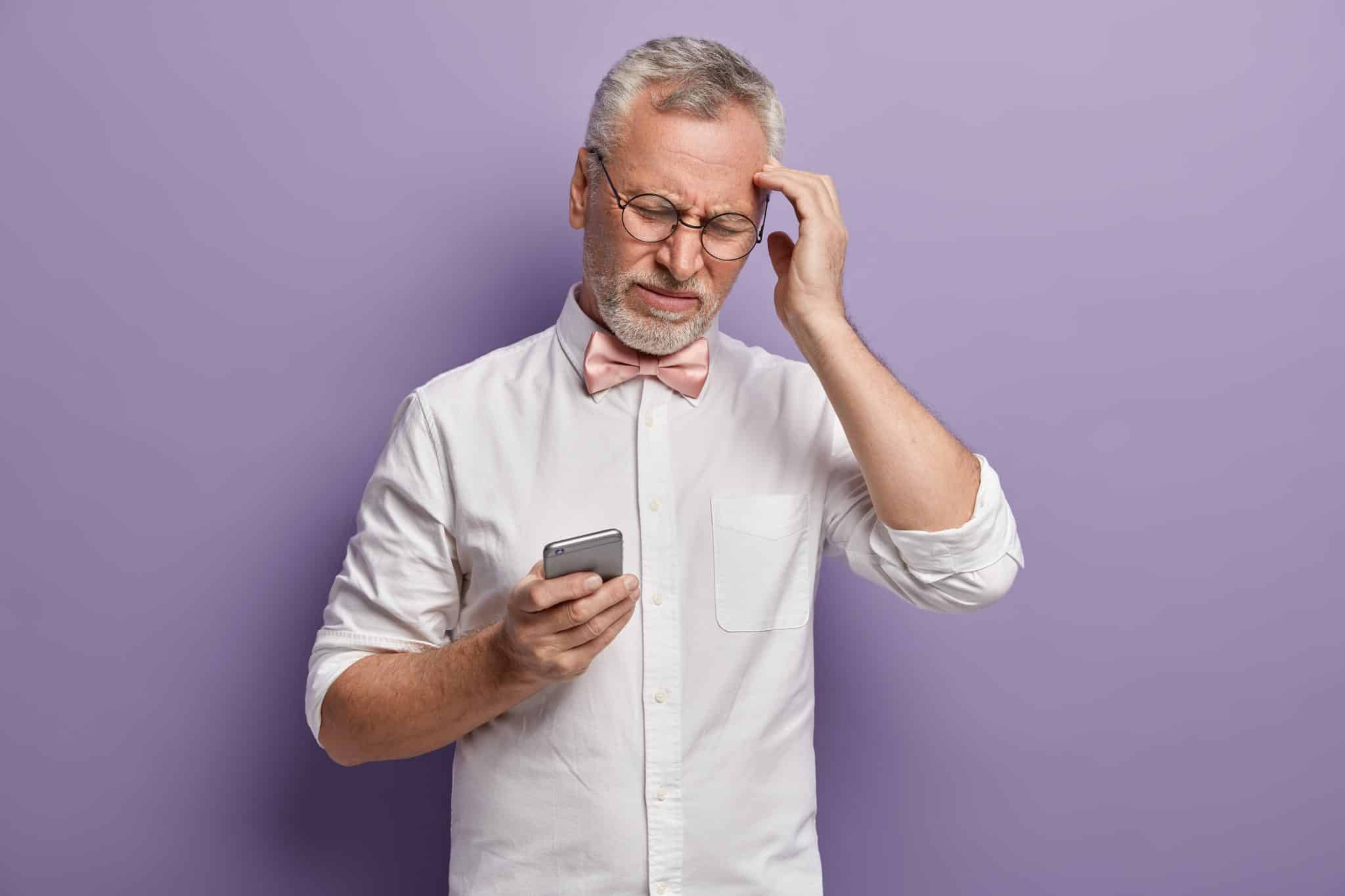 senior man white shirt pink bowtie holding phone